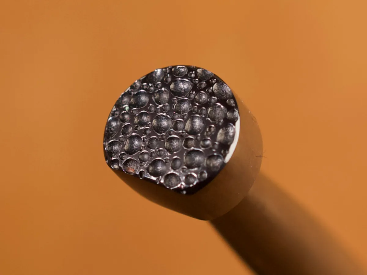 A detailed macro closeup of a backgrounder leatherworking tool with a smooth leather background.
