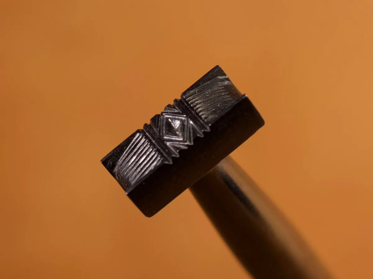 A detailed macro closeup of a basketweave leatherworking tool with a smooth leather background.