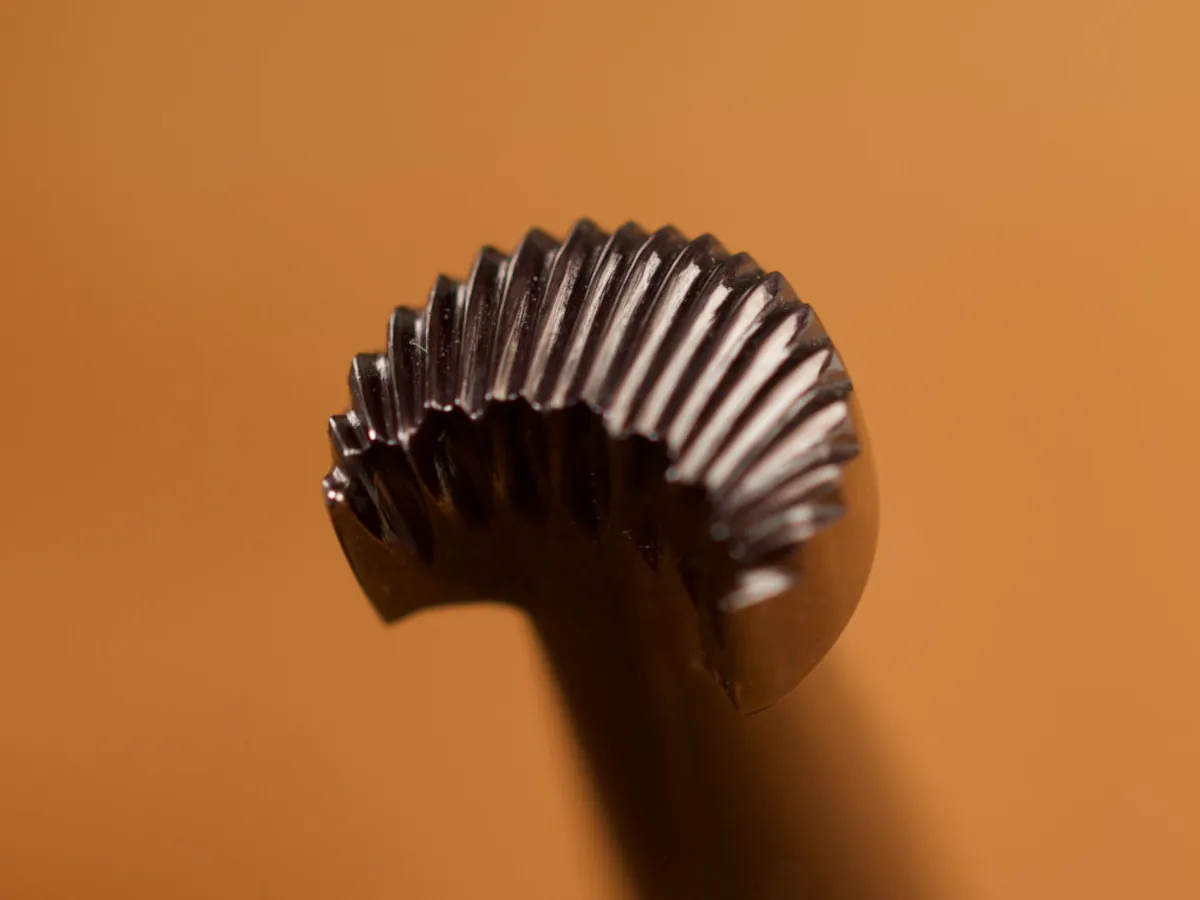 A detailed macro closeup of a camouflage leatherworking tool with a smooth leather background.