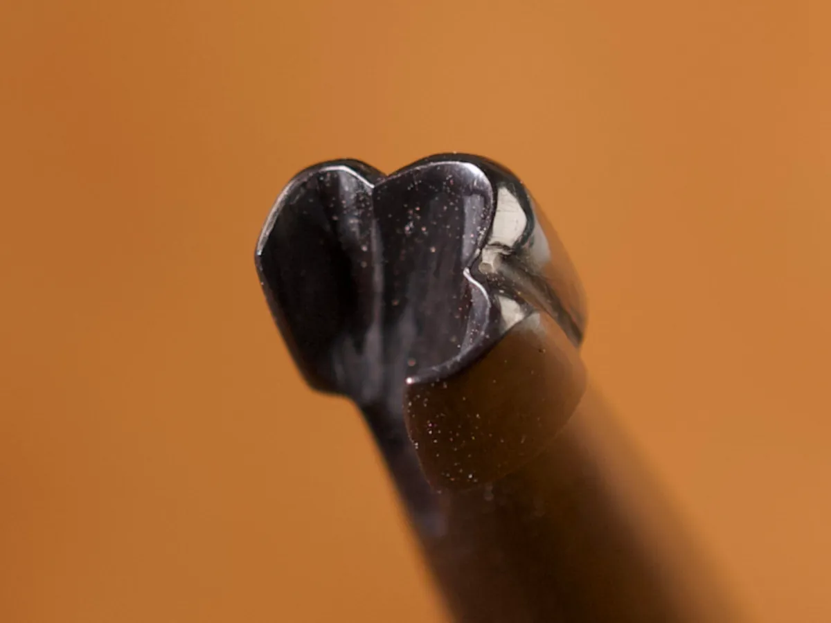 A detailed macro closeup of a flower leatherworking tool with a smooth leather background.