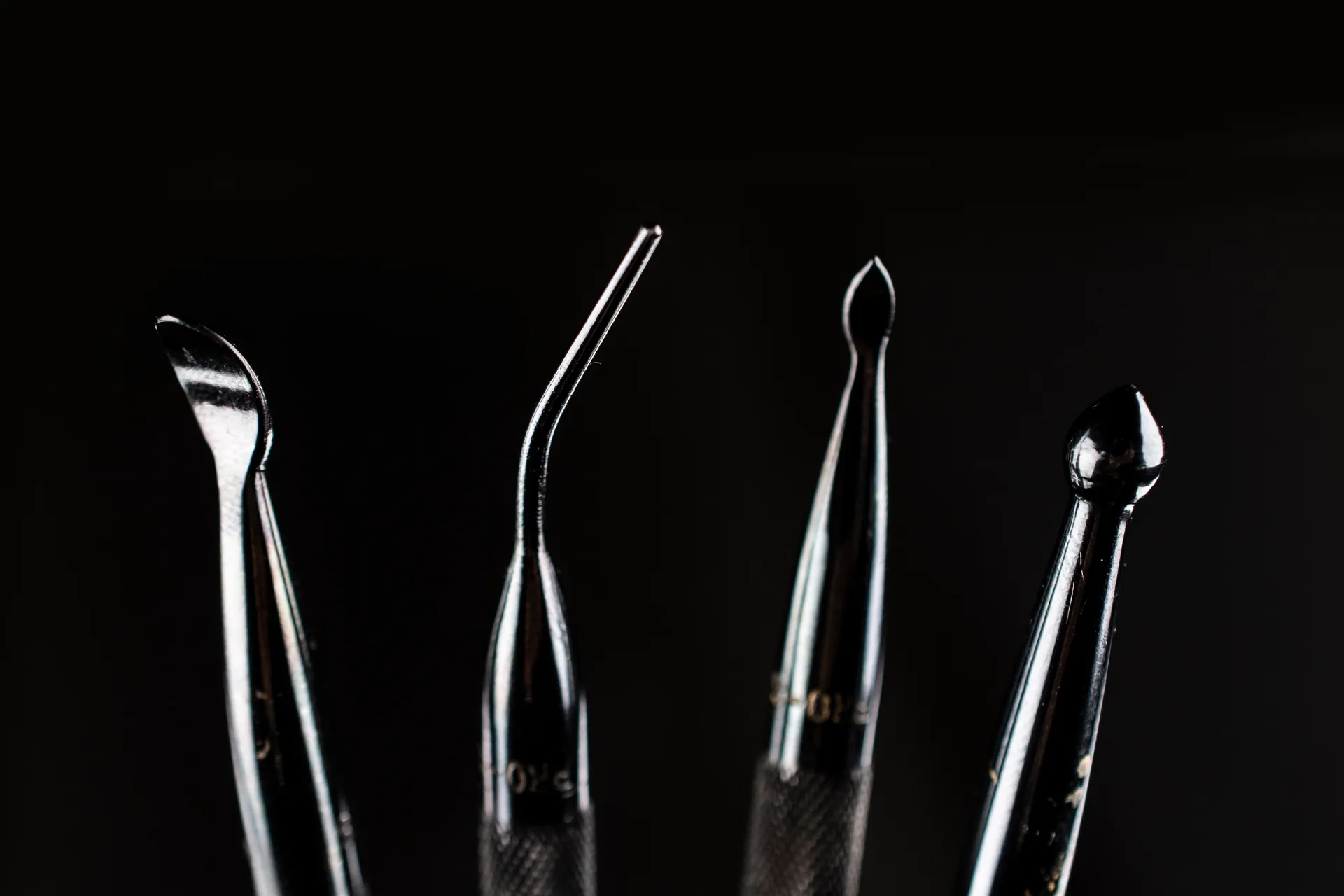 A detailed macro closeup of four stainless steel modelling spoons arranged neatly against a dark, minimalist background.
