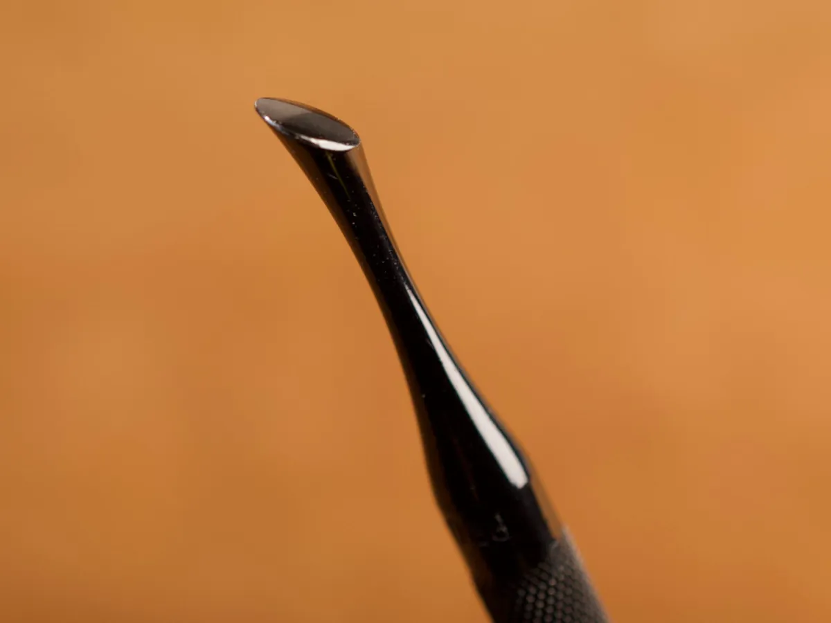 A detailed macro closeup of a modeling spoon leatherworking tool with a smooth leather background.