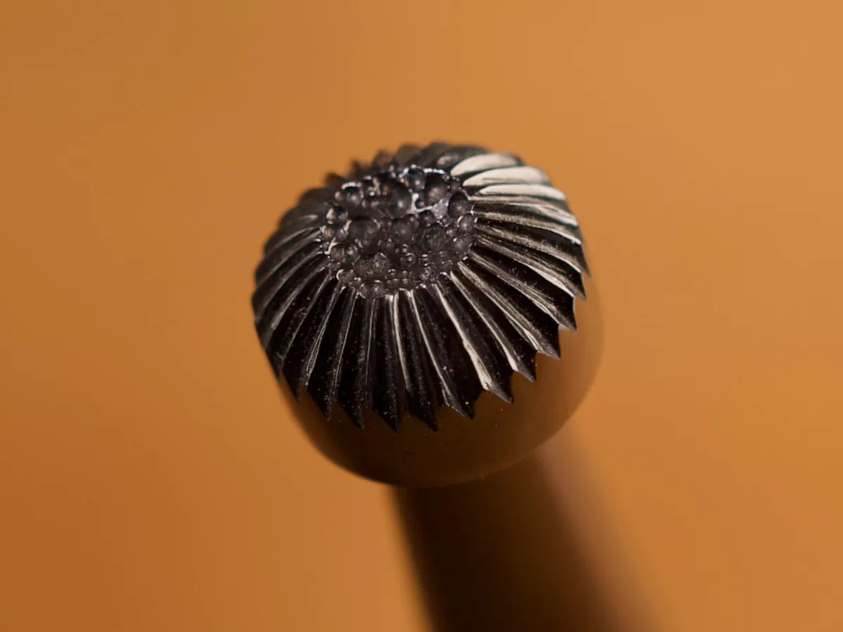 A detailed macro closeup of a seeder leatherworking tool with a smooth leather background.
