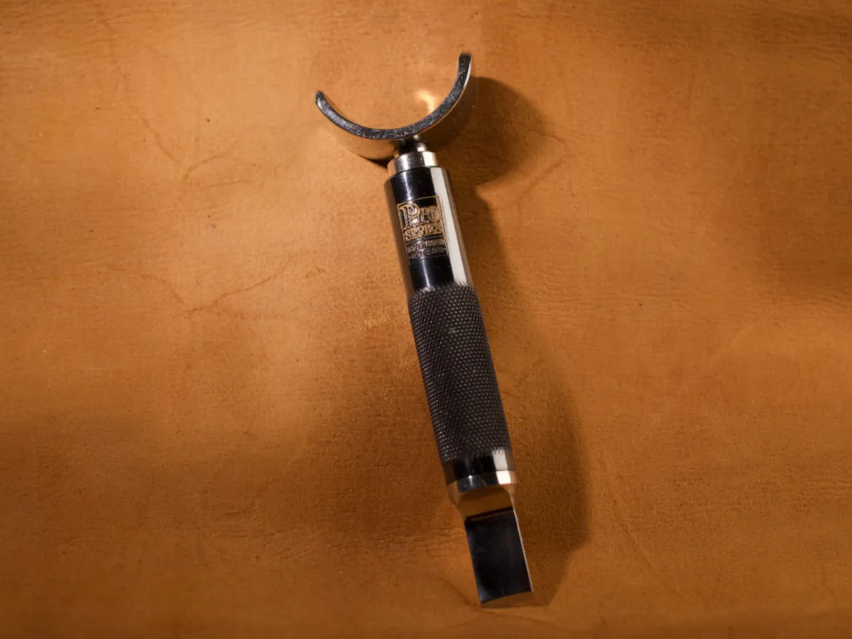 A detailed macro closeup of a swivel knife leatherworking tool with a smooth leather background.