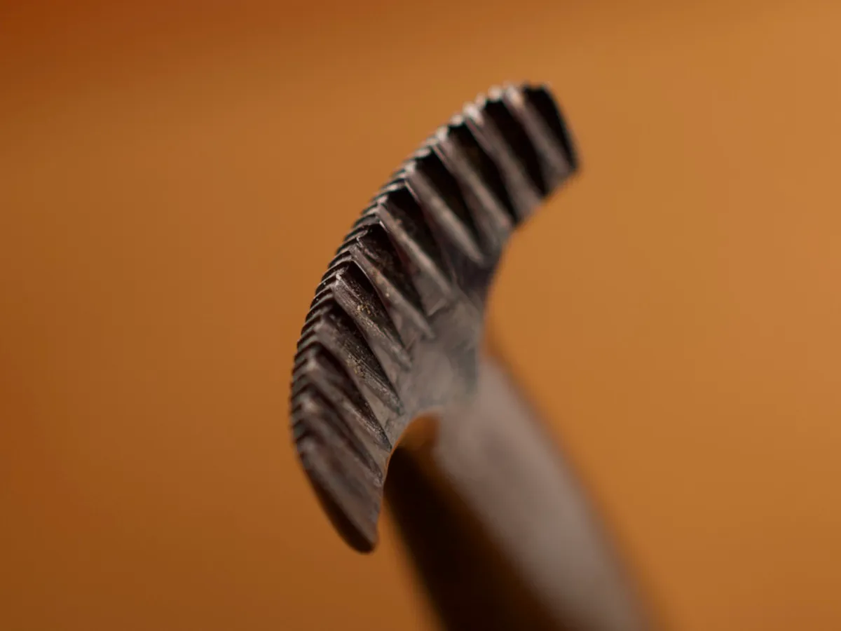 A detailed macro closeup of a veiner leatherworking tool with a smooth leather background.